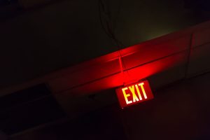 Exit Emergency Light. Red illuminated exit sign glowing in a dimly lit hallway ceiling, symbolizing emergency egress and life safety.
